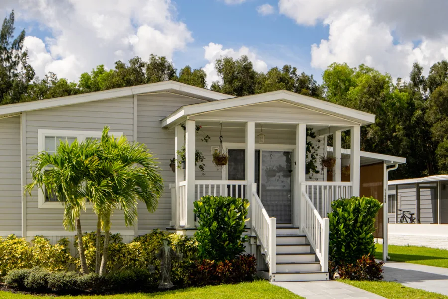 Front view of a gray single-family home with a covered front porch, white railings, and a manicured lawn with tropical plants.