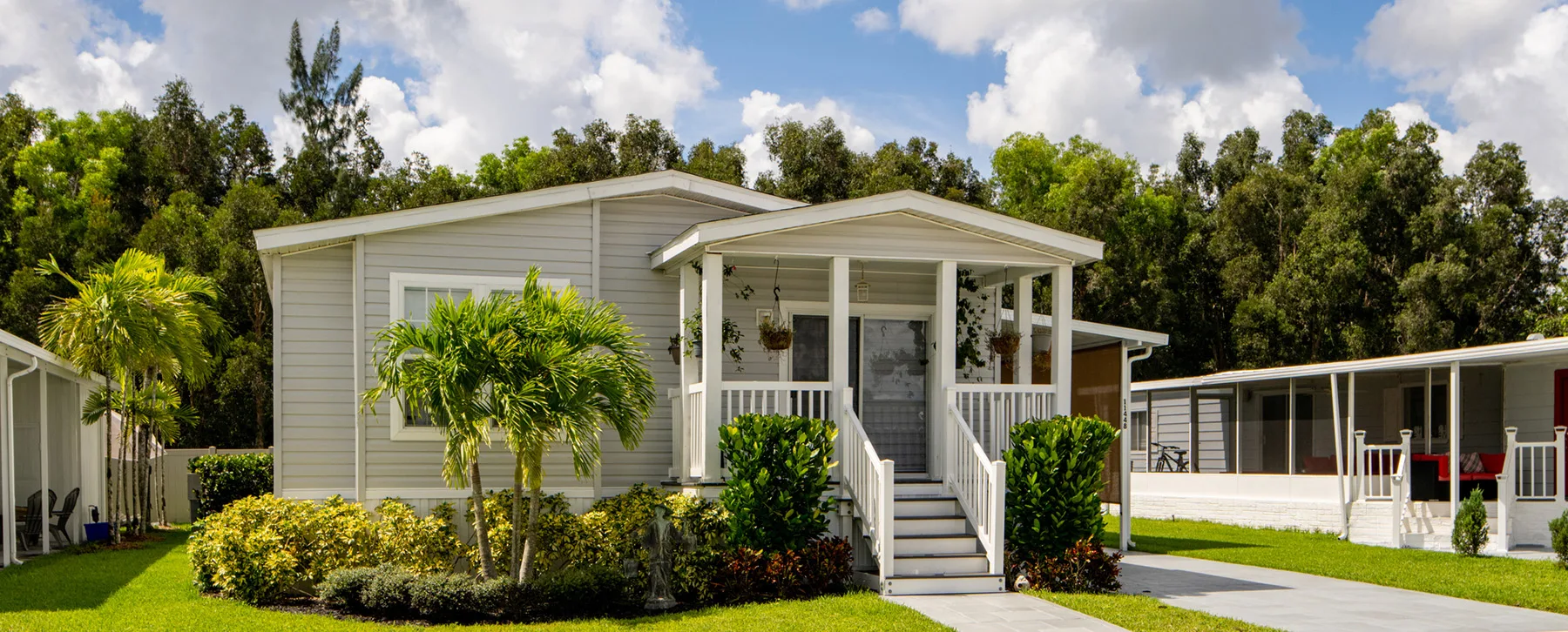 Front view of a gray single-family home with a covered front porch, white railings, and a manicured lawn with tropical plants.