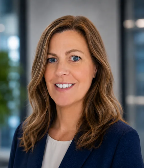 Professional head-and-shoulders portrait of a smiling woman in a navy blazer, in a bright office setting