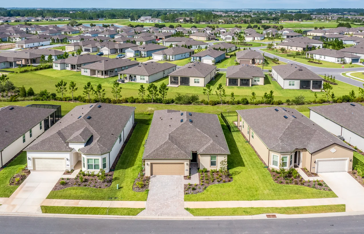 Aerial view of a suburban housing development with rows of single-family homes and green lawns along curved streets.